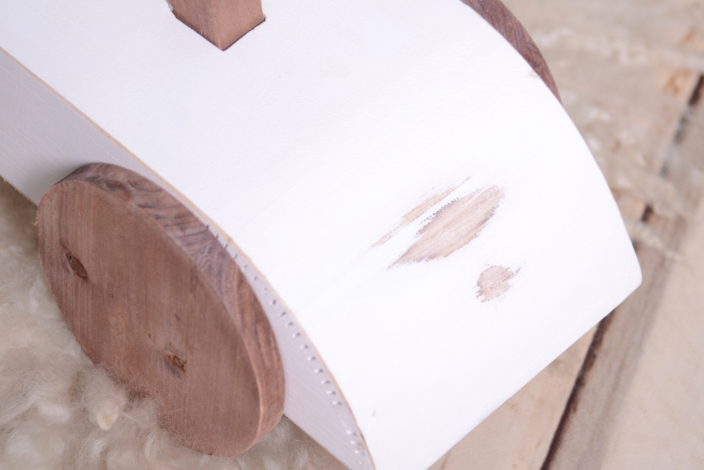 Close-up of the Rustic Ride-On - White's wooden wheel and curved frame, emphasizing its rustic charm as a newborn photography prop.