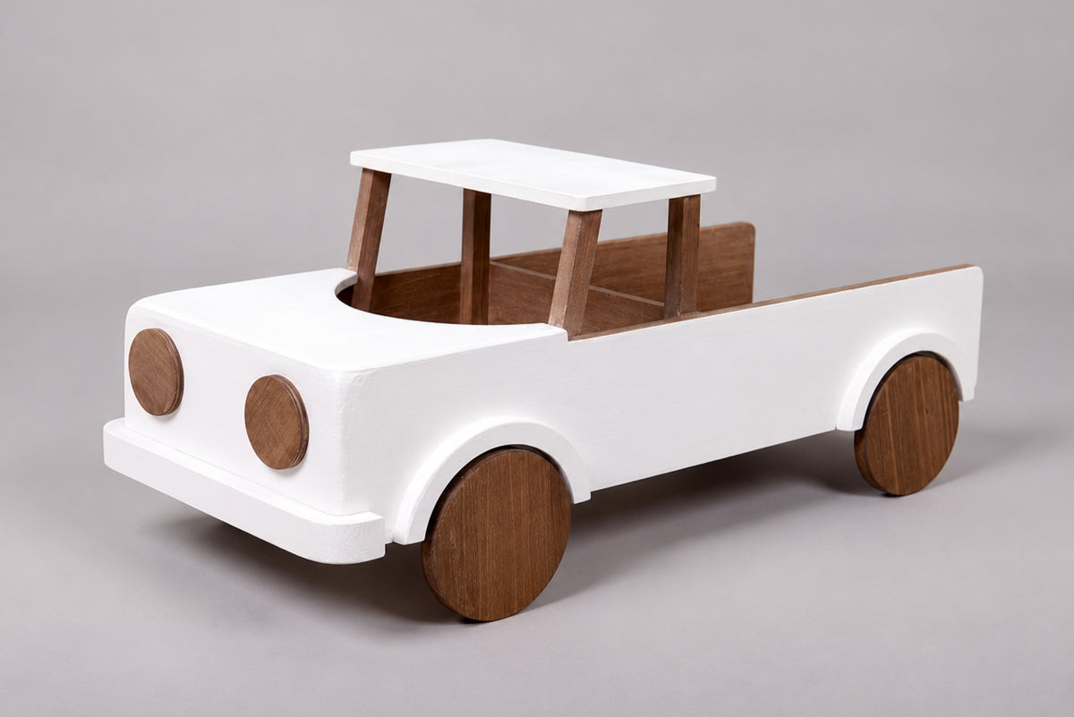 A minimalist wooden toy pickup truck for cake smash photography with a white-painted body and natural brown wood accents for the wheels, bed interior, and canopy,