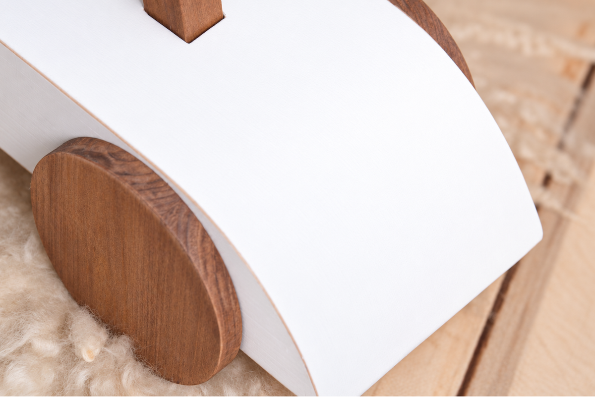 Close-up of the Rustic Ride-On - White's wooden wheel and curved frame, emphasizing its rustic charm as a newborn photography prop.
