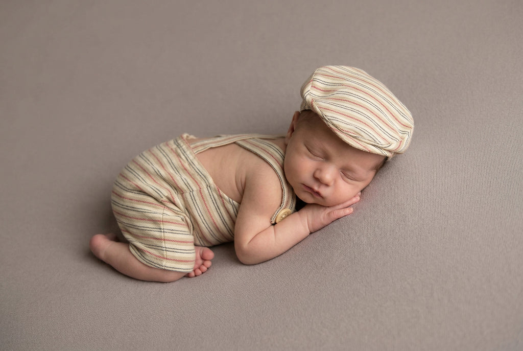 Newborn baby in striped outfit and hat lying on a brown background