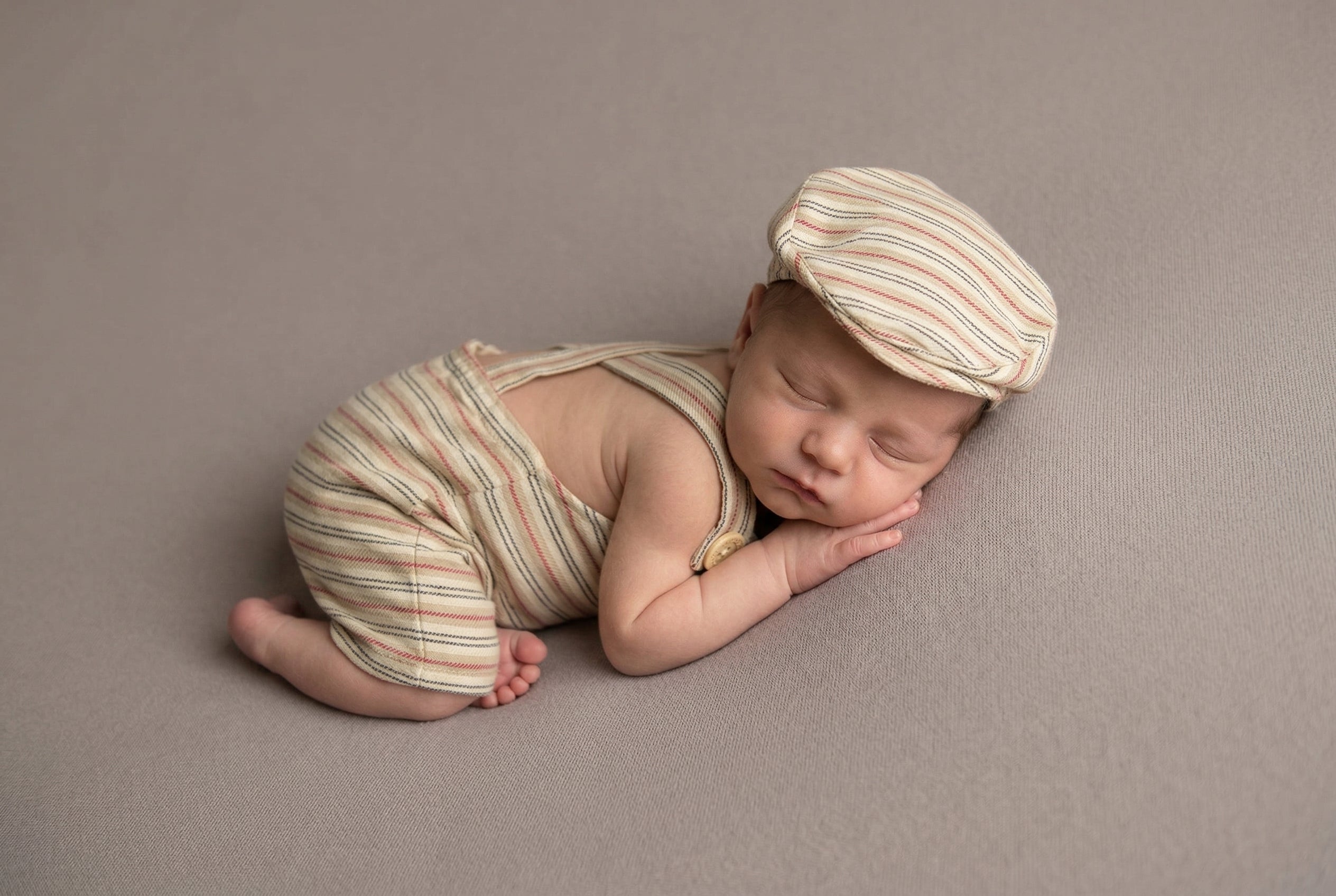 Newborn baby in striped outfit and hat lying on a brown background