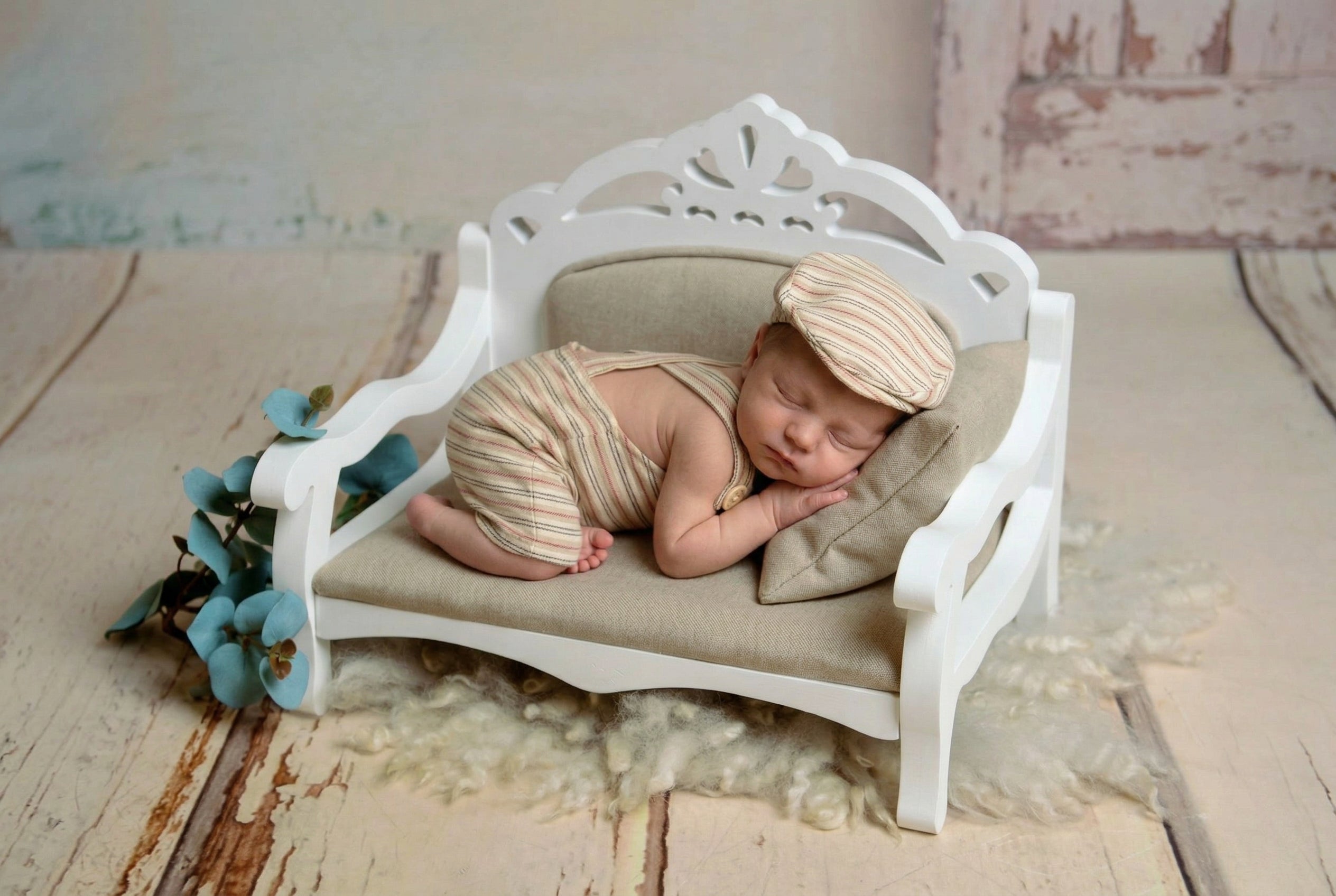 Newborn baby lying on a small white bed with a wooden floor and floral decorations.