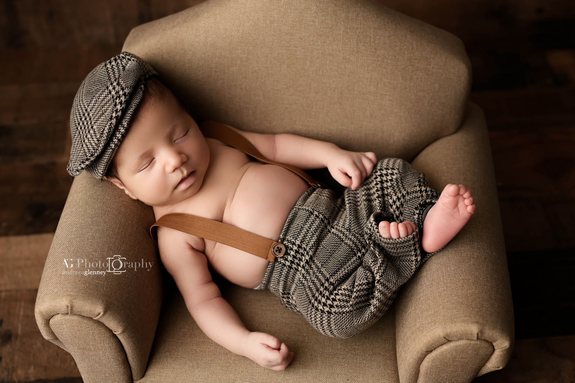Sleeping baby on a light brown mini sofa, wearing a houndstooth hat and pants as a newborn photography prop.