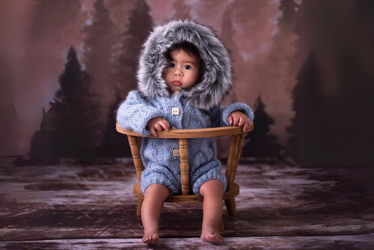 Infant in fuzzy-hooded knitted onesie on a wooden Orbit Chair, a cozy newborn photography prop.