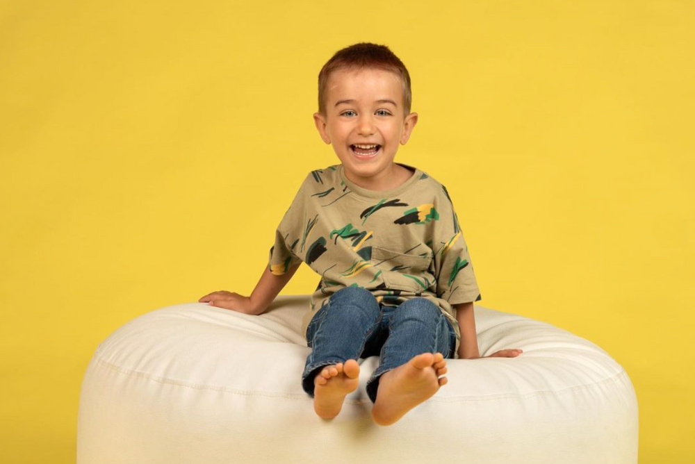 Smiling baby on a white photography prop beanbag with a bright yellow backdrop.