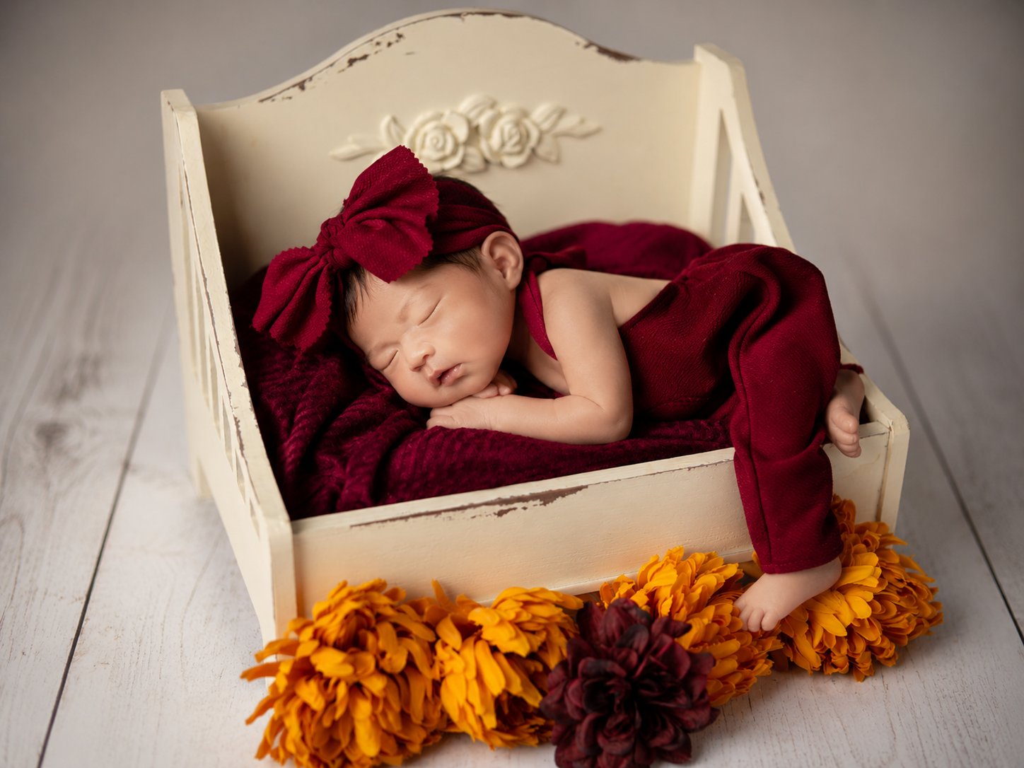 Newborn baby in a red outfit and bow sleeping in a white crib in a newborn photography studio setup