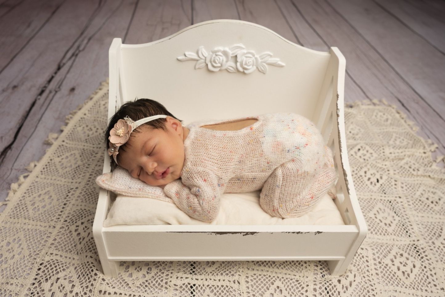 Newborn asleep on a white vintage daybed, cozy in a knit wrap, newborn photography prop.