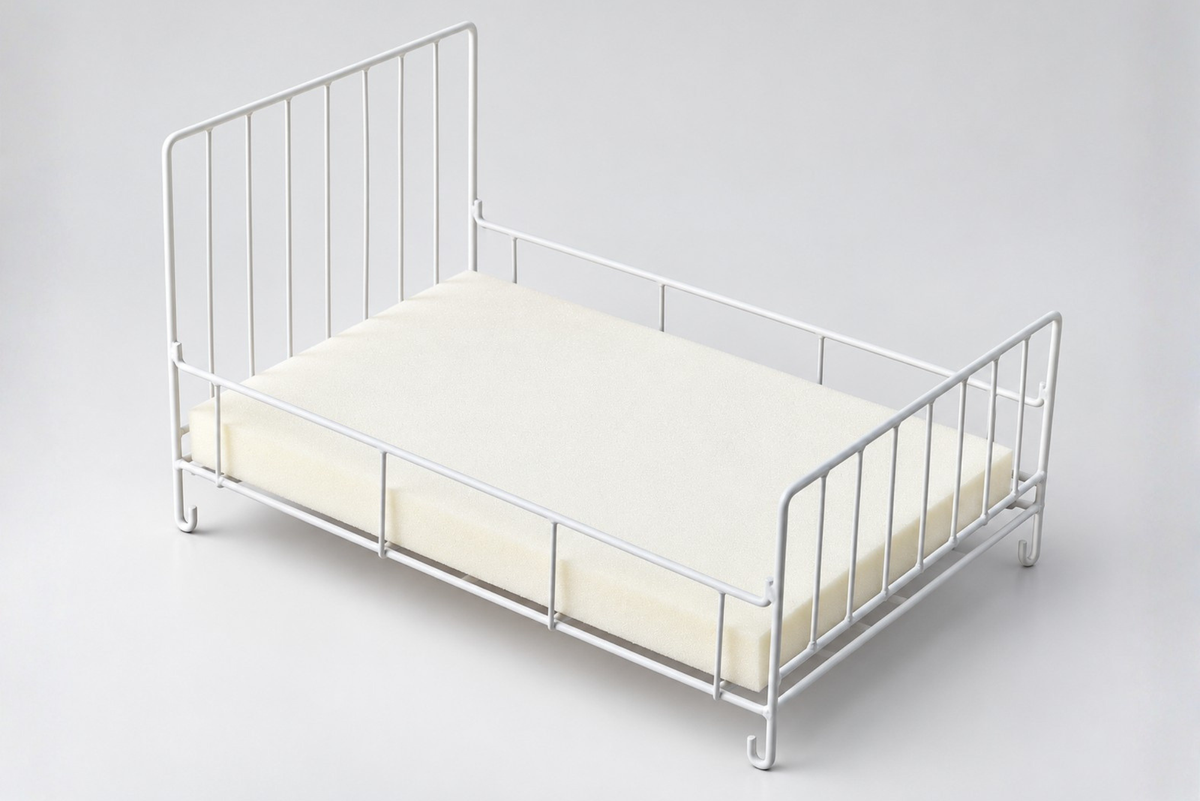 White metal newborn photography prop bed with a minimalist wire frame, inward-facing curved legs, and cream foam mattress, photographed on a light gray studio background.
