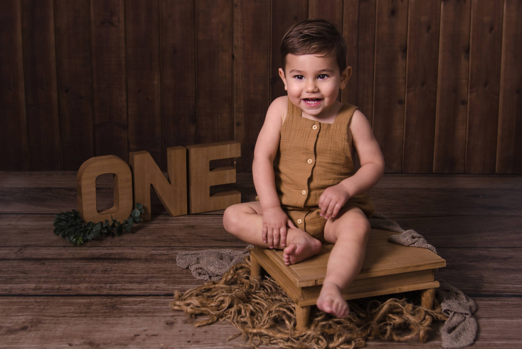 Milestone Session Smiling baby on rustic wooden platform with “ONE” sign, styled with neutral newborn photography prop setup.