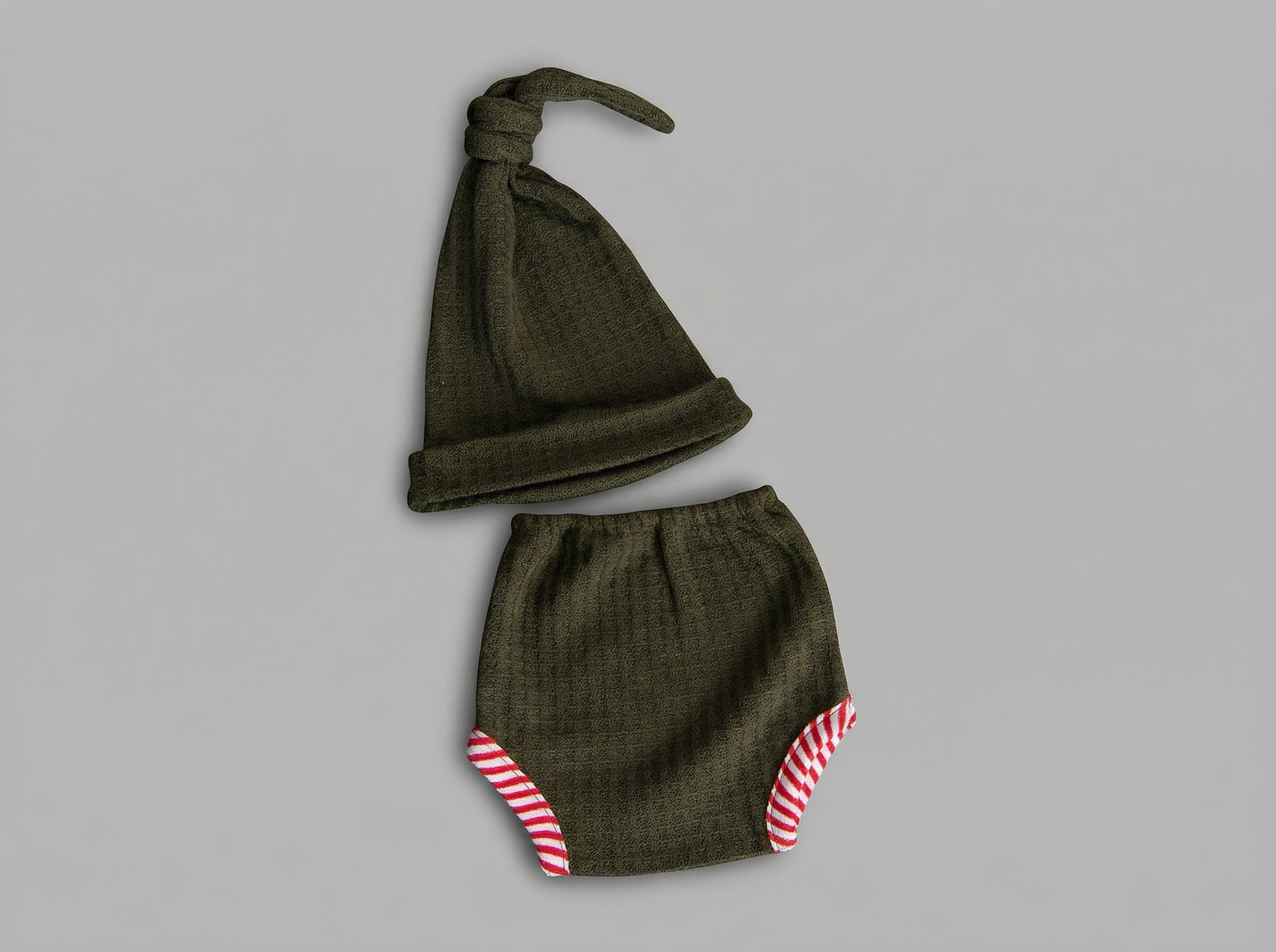 Green baby hat and diaper set with red and white trim on a gray background