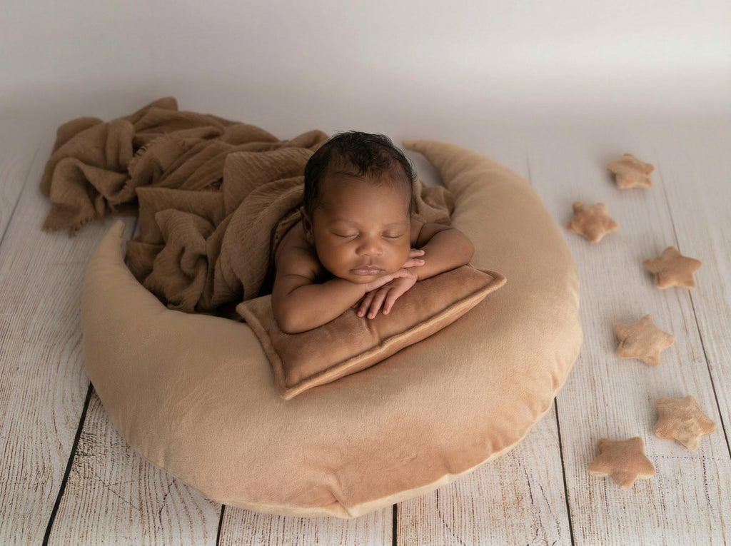 Newborn baby wrapped in a brown blanket on a heart-shaped pillow with star-shaped objects around.
