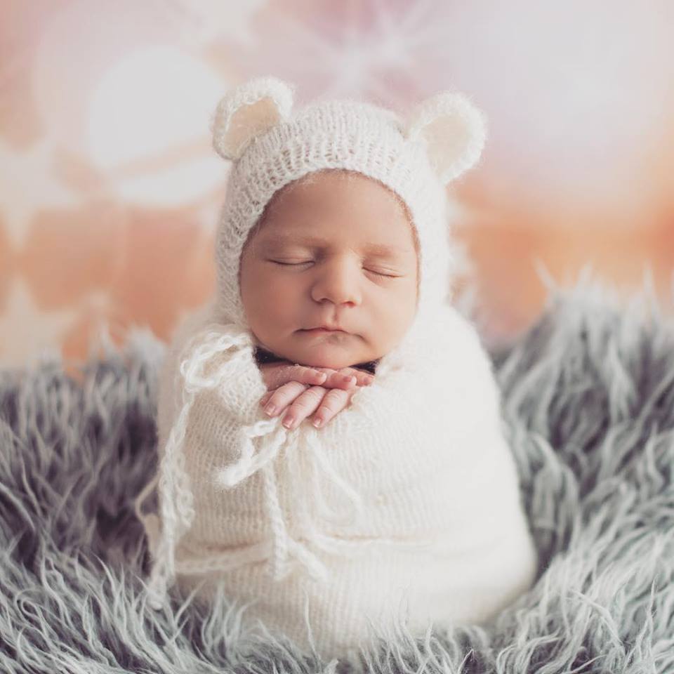 Serene newborn in a white mohair bear bonnet and sack, resting on a textured cream backdrop, exemplifying a cozy and peaceful newborn photography prop setup."