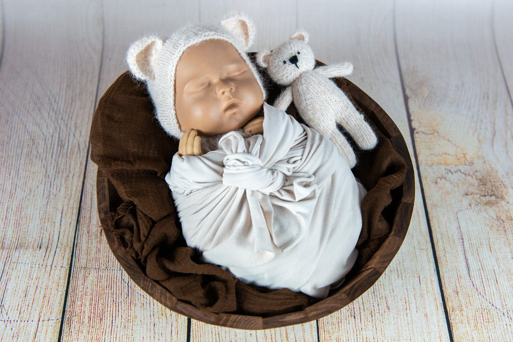 Knit teddy bear and matching hat beside cream swaddle; newborn photography prop.