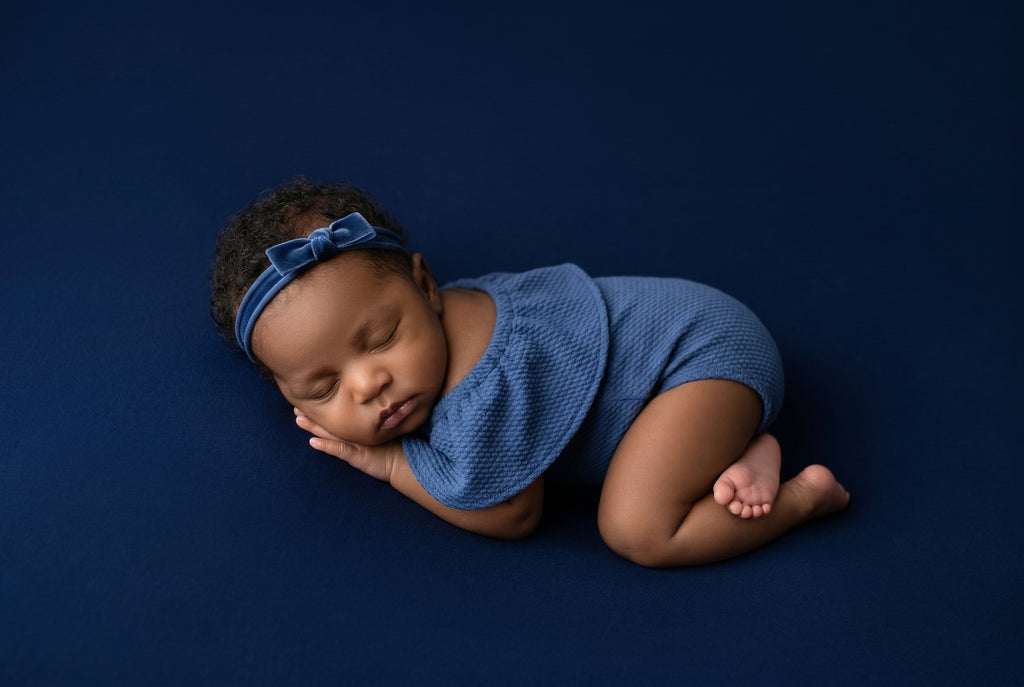 Newborn baby wearing a blue outfit and headband on a dark blue background