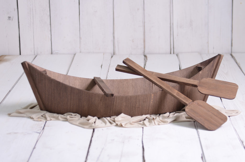 Rustic wooden canoe with paddles, a charming newborn photography prop on white wood floor.