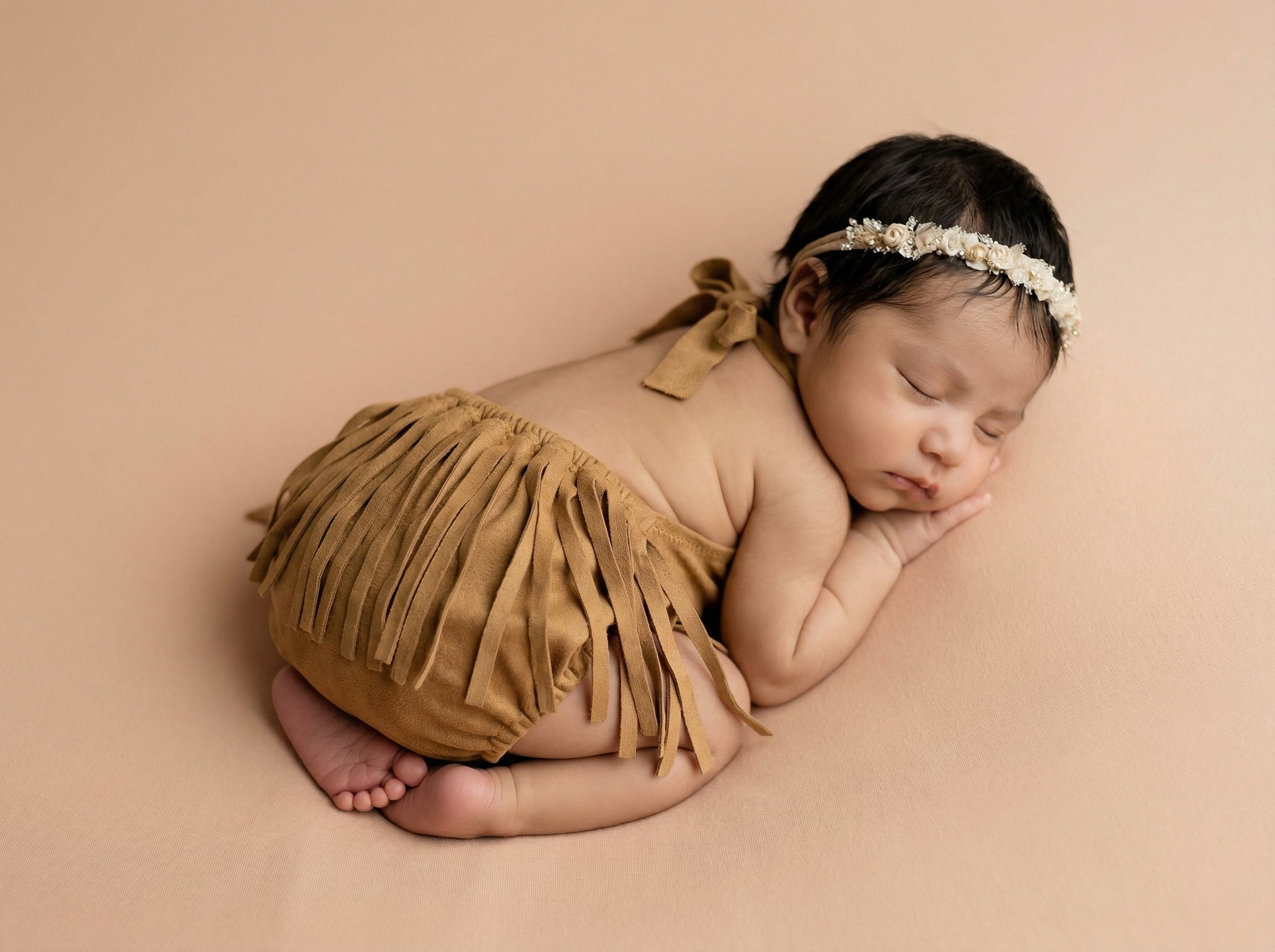 Newborn baby in a mustard fringed suede romper and headband