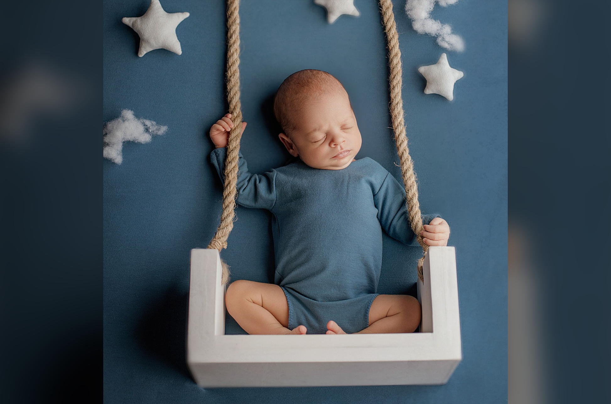 Newborn asleep on a white rustic swing prop, wearing a knit prop outfit. 