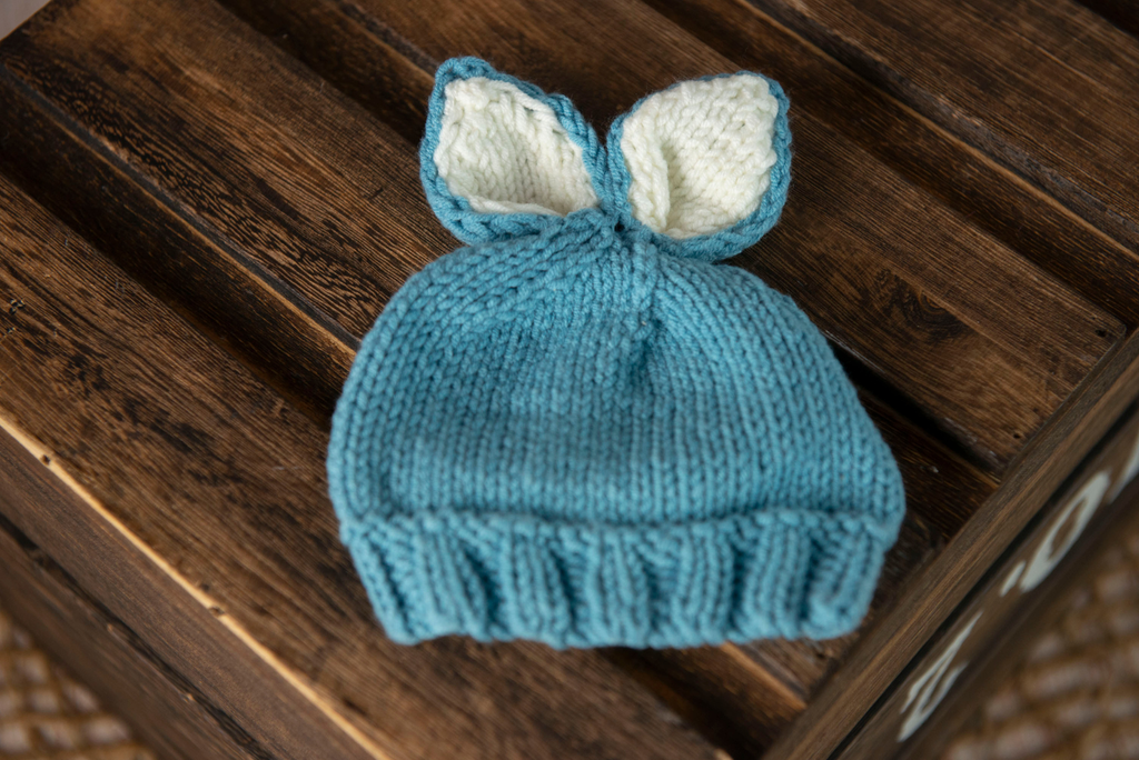 Blue knitted baby hat with white ears on a wooden surface