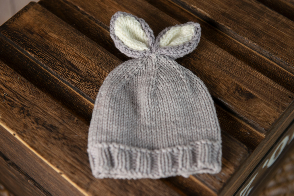 Knitted baby hat with bunny ears on a wooden surface