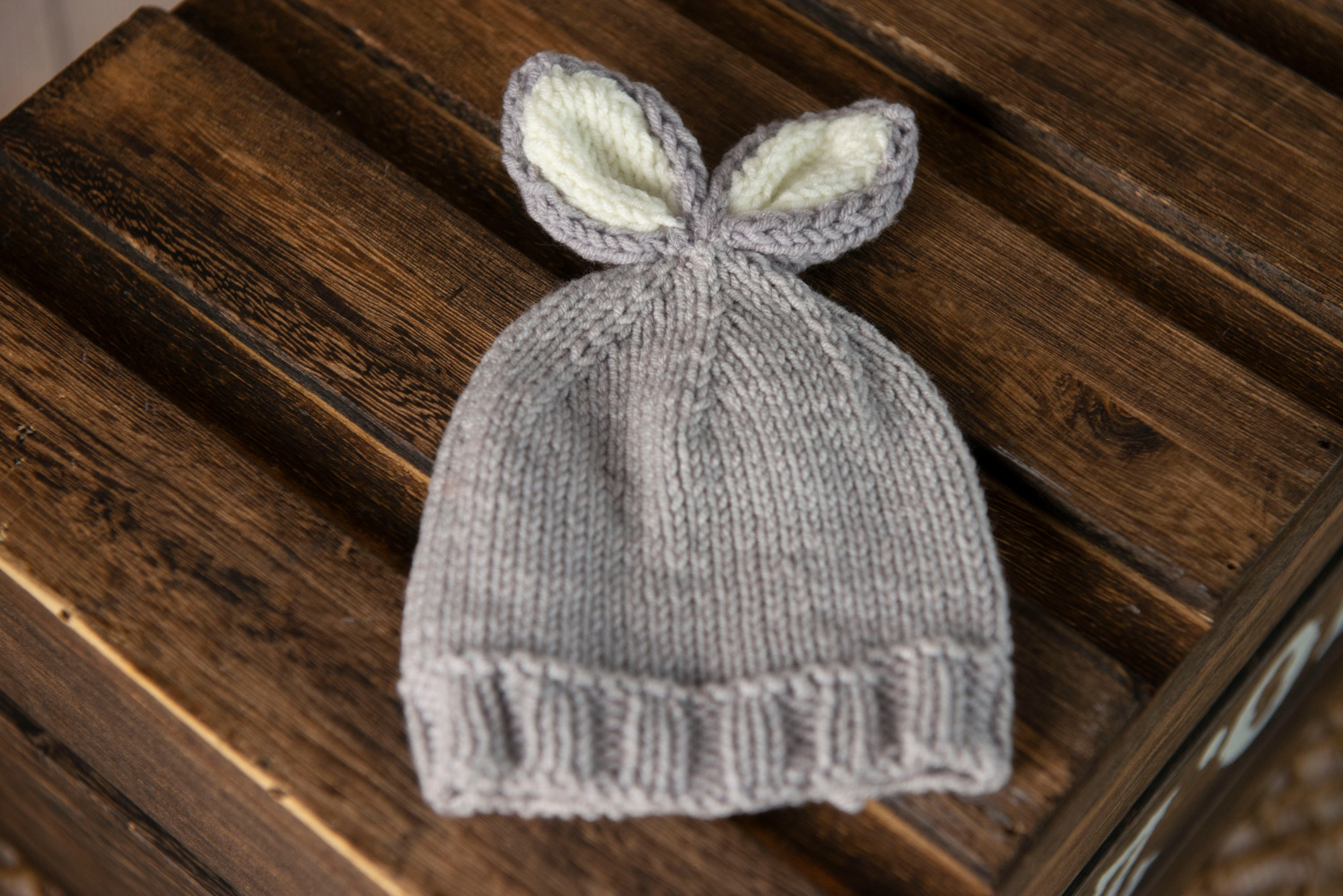 Knitted baby hat with bunny ears on a wooden surface