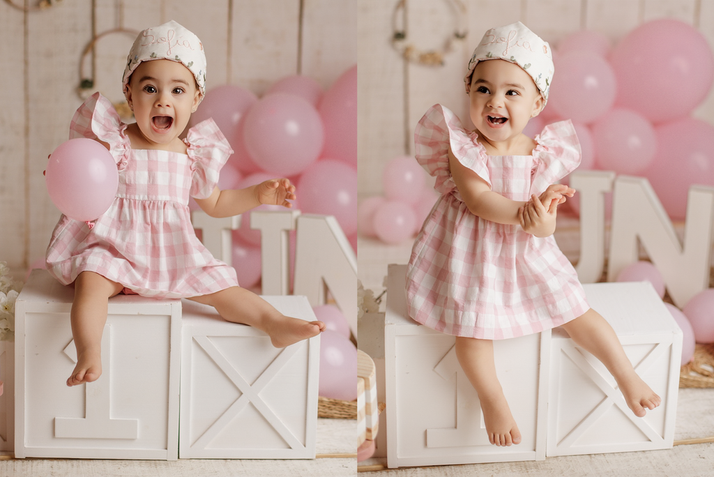 Smiling baby girl sits on white “ONE” cake smash boxes, a classic newborn photography prop with pink balloons in milestone session.