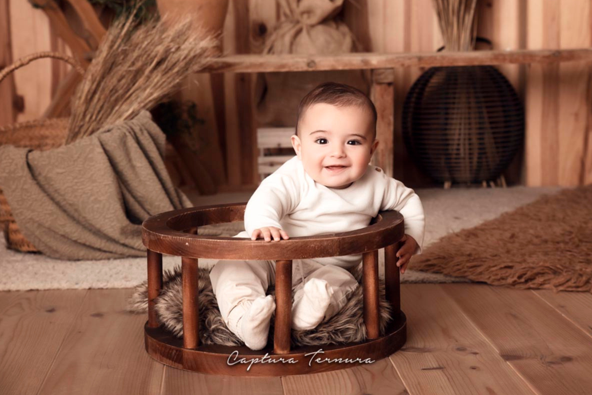 Baby in white outfit sitting in wooden circular seat newborn photography prop with faux fur and rustic backdrop.