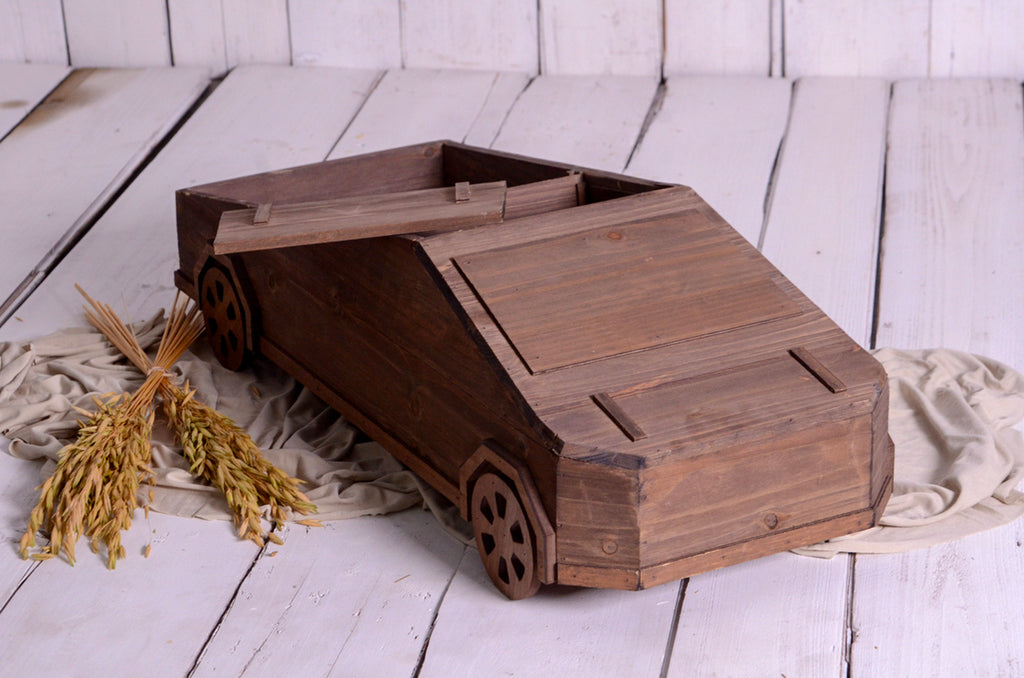 Side view of newborn photography prop styled as a tesla cybertruck with lifted lid and rustic wheat accent.