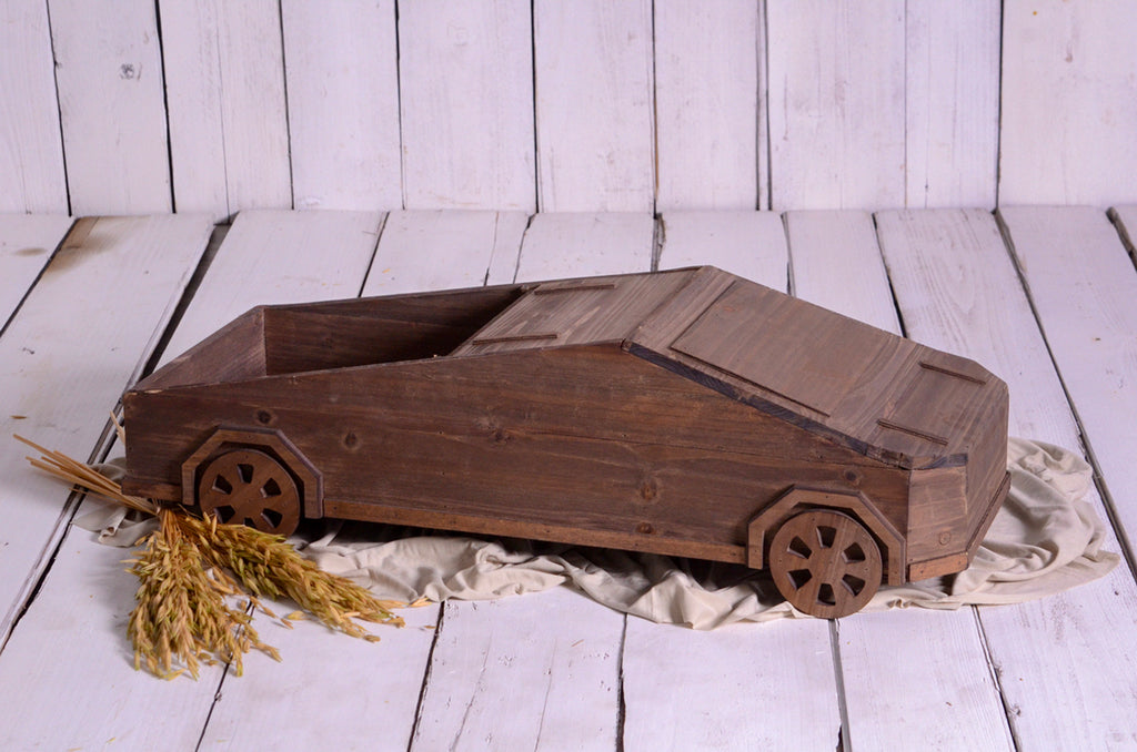 Rustic wooden car-shaped newborn photography prop on white wood floor with wheat and fabric.