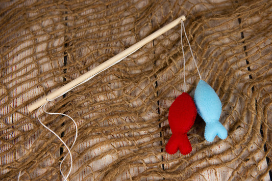 A faux fishing rod with red and blue felt fish on a rustic net, ideal for newborn photography prop setups.