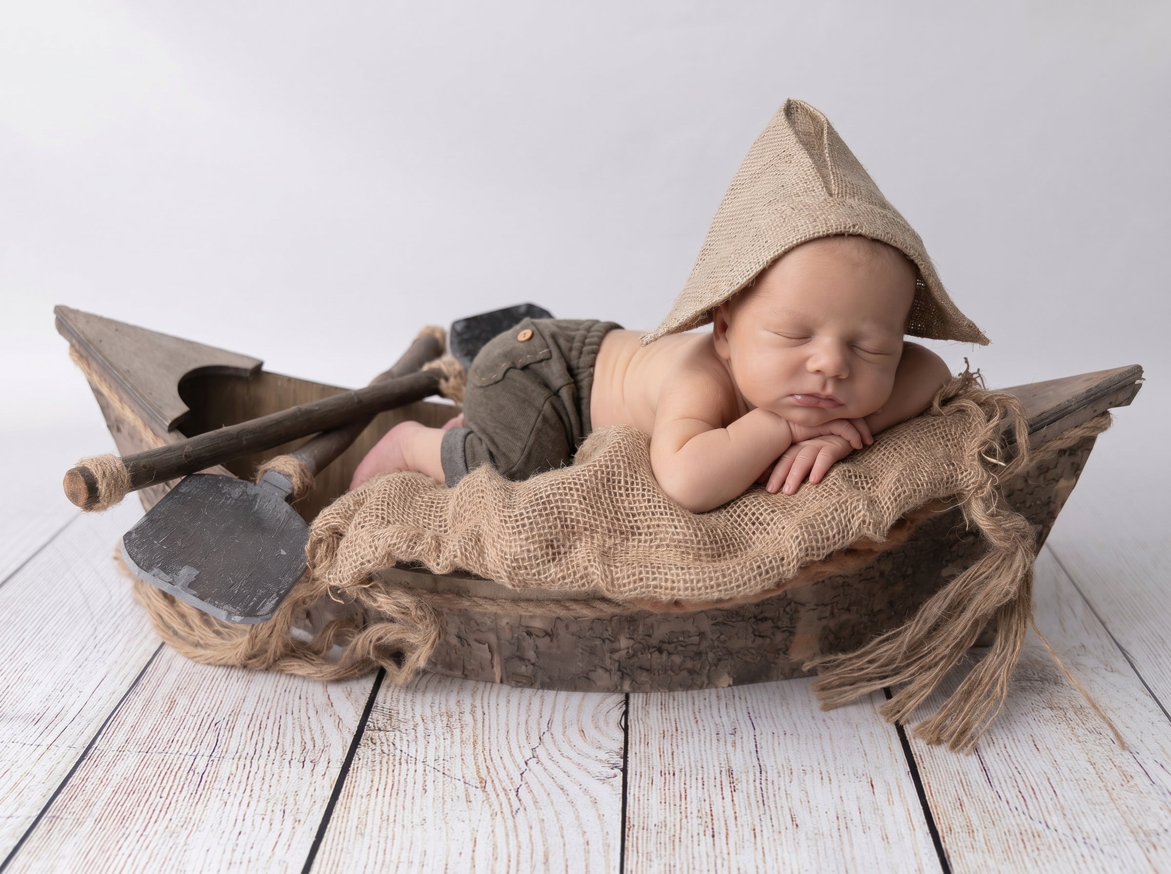 Newborn baby in a wooden boat prop with a fisherman's hat and pants