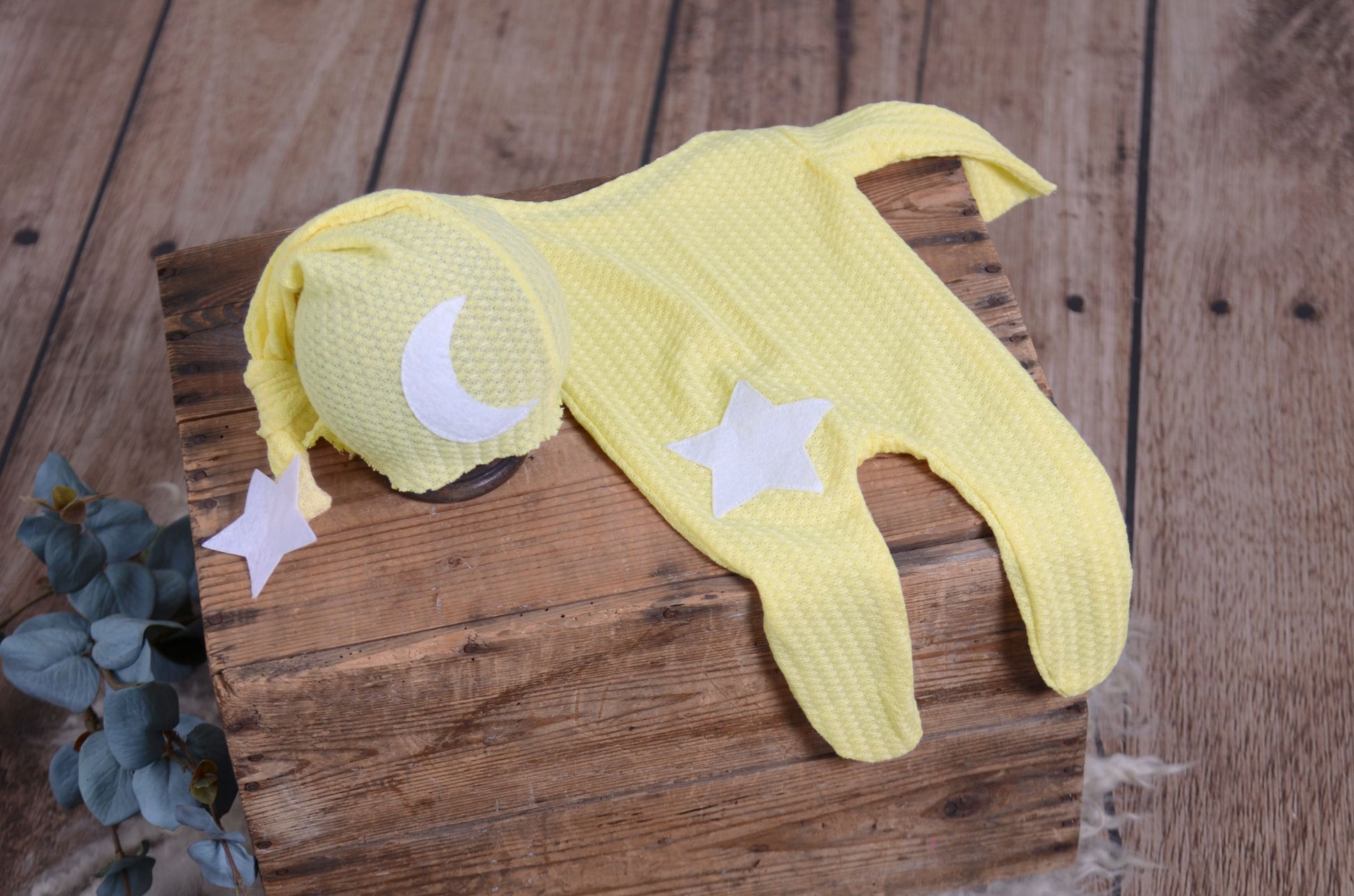 Yellow waffle fabric footed pajamas and matching hat with moon and stars, displayed as a newborn photography prop on a rustic wooden surface.