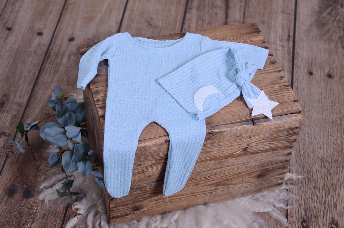 Light Blue waffle fabric footed pajamas and matching hat with moon and stars, displayed as a newborn photography prop on a rustic wooden surface.