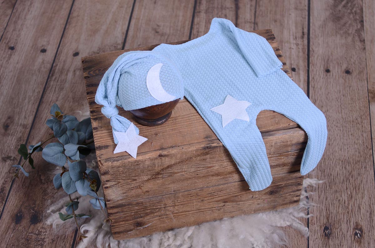 Light Blue waffle fabric footed pajamas and matching hat with moon and stars, displayed as a newborn photography prop on a rustic wooden surface.