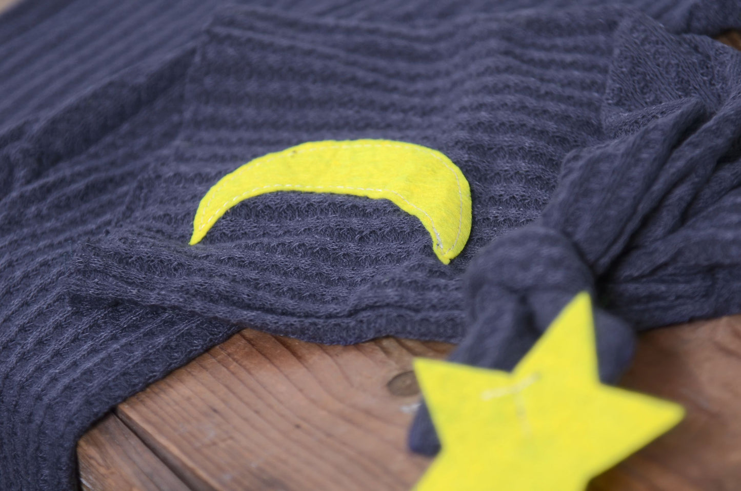 Blue waffle fabric footed pajamas and matching hat with moon and stars, displayed as a newborn photography prop on a rustic wooden surface.