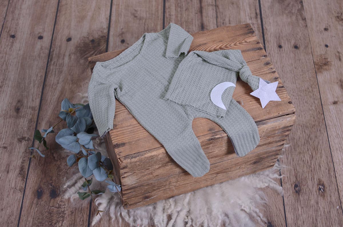 Silver gray waffle fabric footed pajamas and matching hat with moon and stars, displayed as a newborn photography prop on a rustic wooden surface.