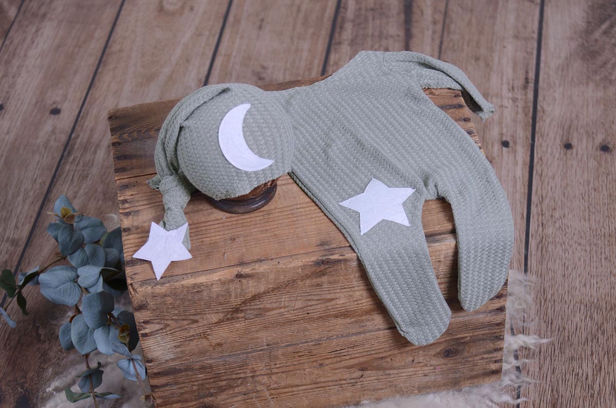 Silver gray waffle fabric footed pajamas and matching hat with moon and stars, displayed as a newborn photography prop on a rustic wooden surface.