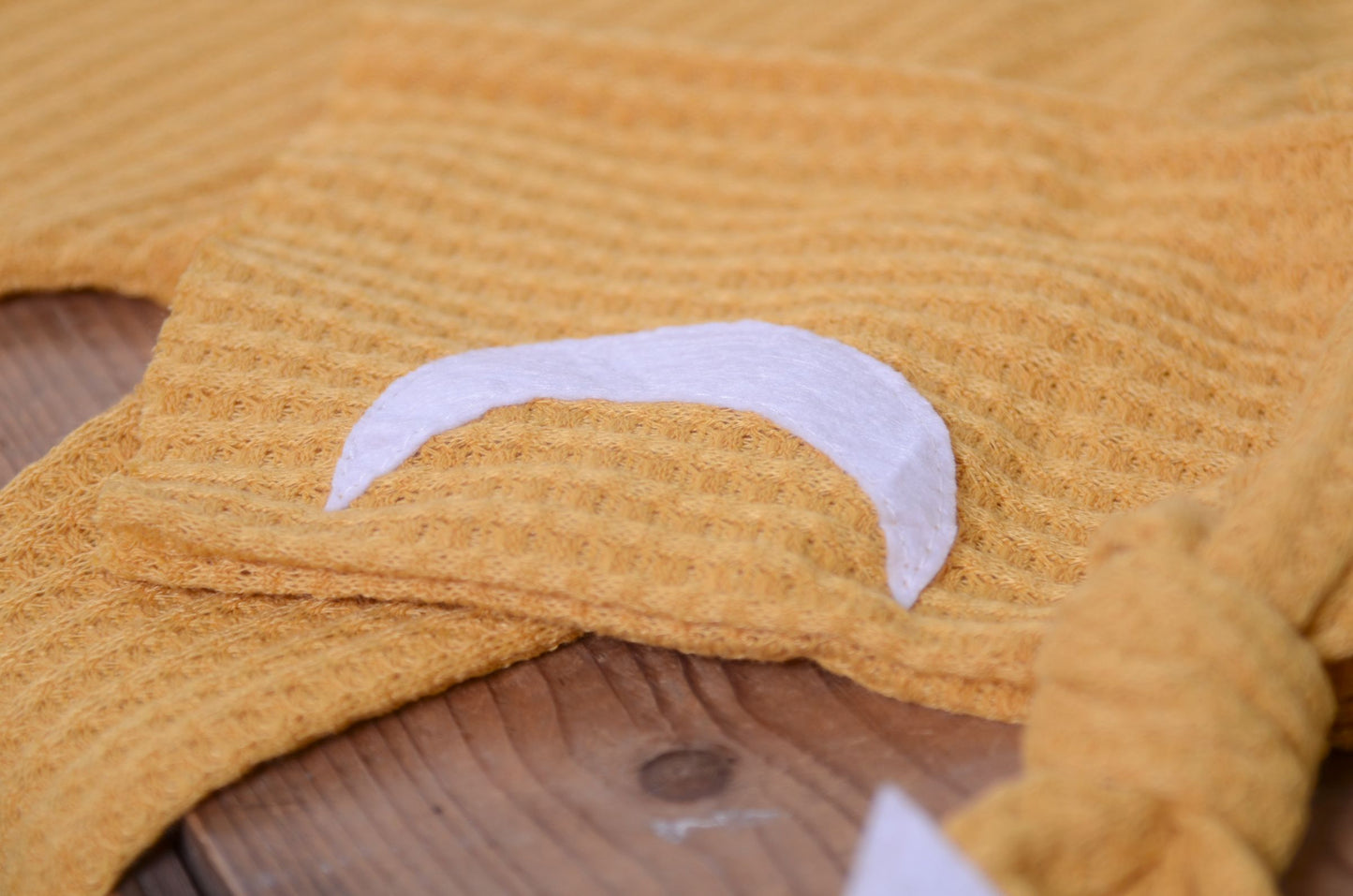 Mustard waffle fabric footed pajamas and matching hat with moon and stars, displayed as a newborn photography prop on a rustic wooden surface.