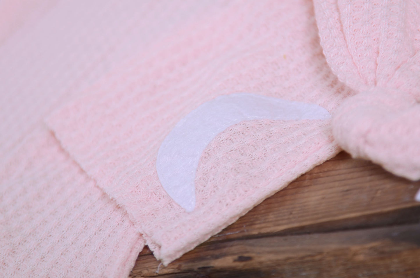 Pink waffle fabric footed pajamas and matching hat with moon and stars, displayed as a newborn photography prop on a rustic wooden surface.