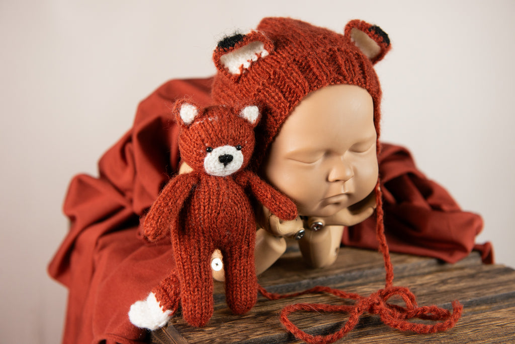 Newborn snuggled in dark orange wrap, with fox bonnet and matching plush, ideal for a warm-toned newborn photography prop setup.