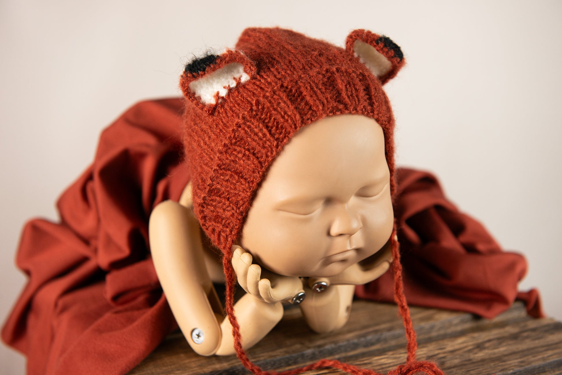 Newborn snuggled in dark orange wrap, with fox bonnet and matching plush, ideal for a warm-toned newborn photography prop setup.