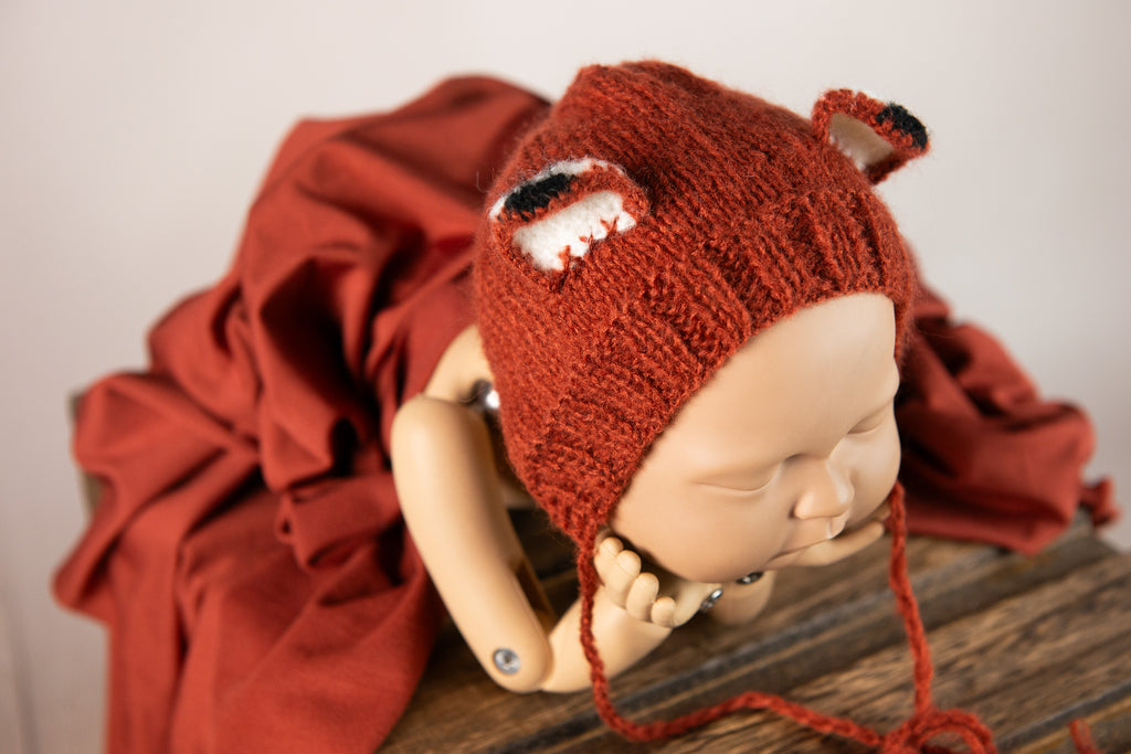 Newborn snuggled in dark orange wrap, with fox bonnet and matching plush, ideal for a warm-toned newborn photography prop setup.