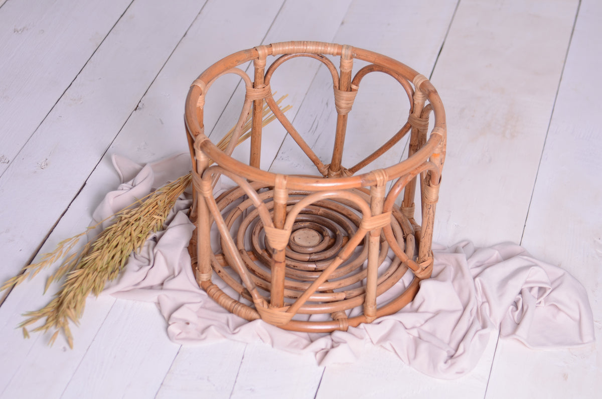 The LovePod rattan basket, a beautifully handcrafted newborn photography prop, sits on a white wooden floor with soft fabric.