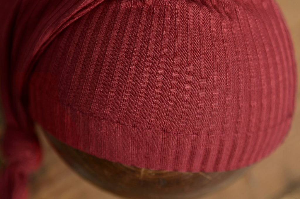 Closeup of ribbed knot sleepy cap newborn photography prop in deep burgundy