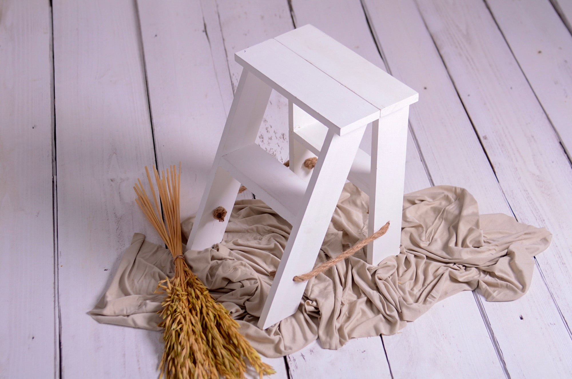 Rustic mini step ladder prop styled with beige fabric and wheat, ideal for cakesmash photo shoots.