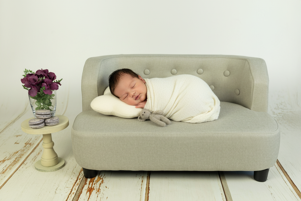 Newborn wrapped in cream blanket sleeps on mini sofa newborn photography prop with toy bunny.
