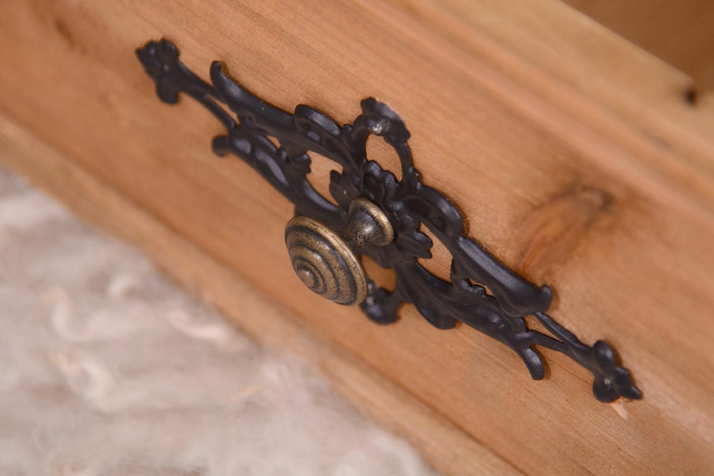 Rustic wooden box prop adorned with an ornate black latch, accompanied by delicate white fluff and a trailing green plant, set against a textured white backdrop. Perfect for newborn photography sessions. Available at Newborn Studio Props.