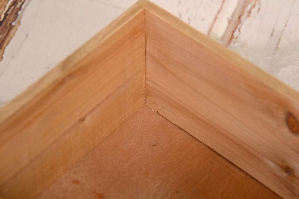 Rustic wooden box prop adorned with an ornate black latch, accompanied by delicate white fluff and a trailing green plant, set against a textured white backdrop. Perfect for newborn photography sessions. Available at Newborn Studio Props.