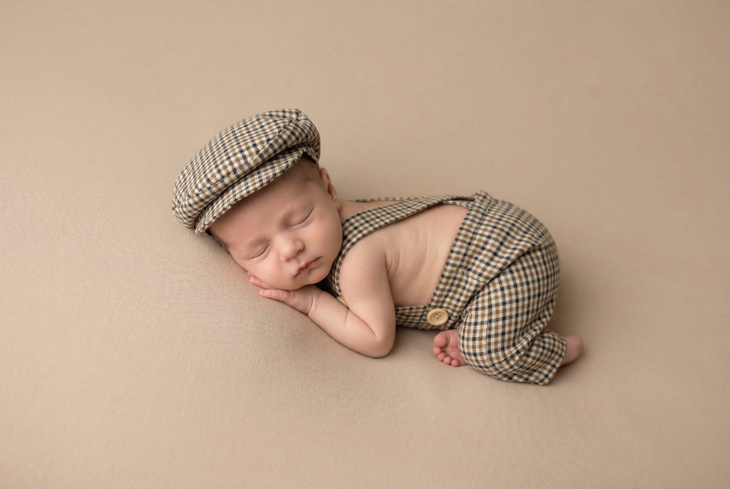 Newborn baby in plaid outfit and cap on a beige background