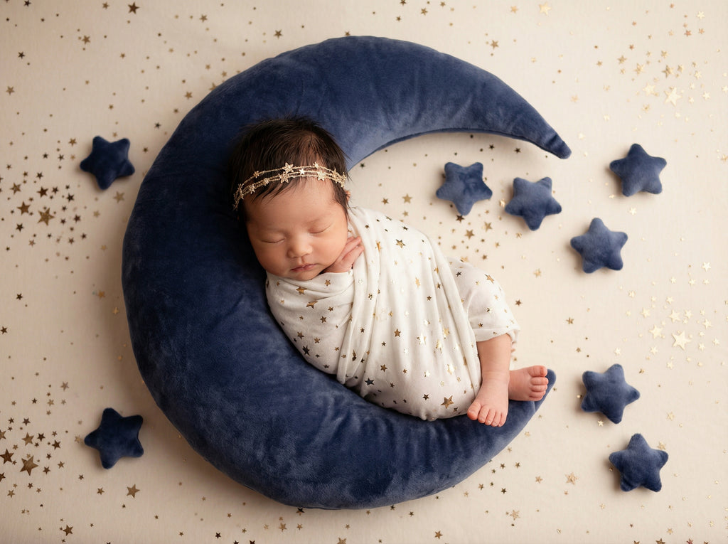 Newborn baby sleeping on a blue crescent moon pillow with star decorations.