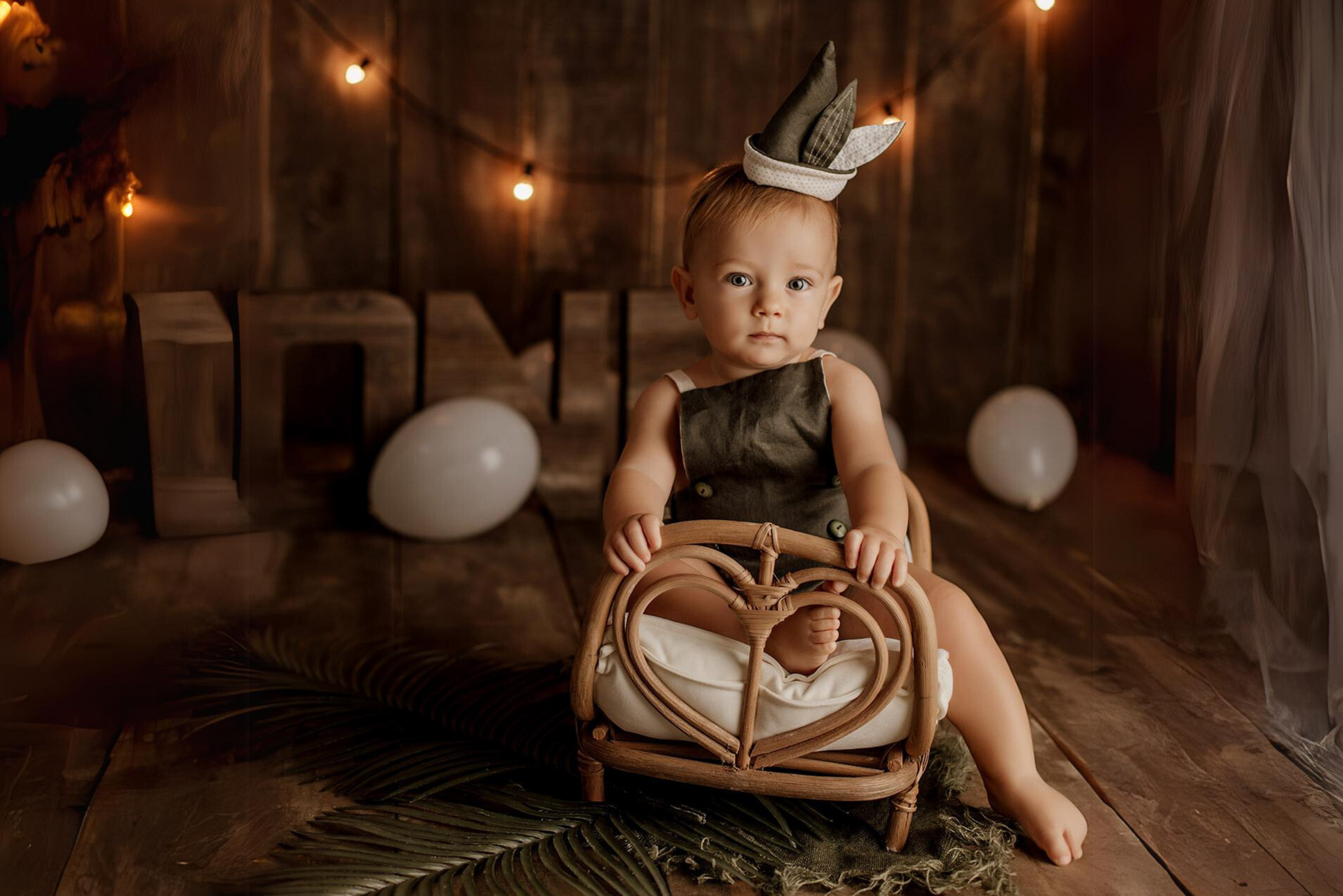 A baby sits in a 'Rattan Love Nest Bed' prop, crowned with a tiny sailor hat, creating a serene mood in this newborn photography setup.